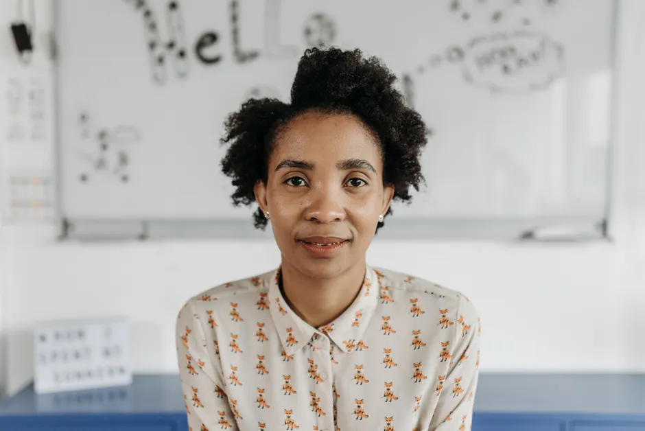 A confident woman with afro hair poses in a classroom, fostering an educational theme.