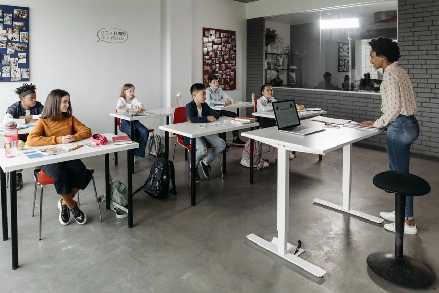A diverse group of students attentively listens to a teacher in a modern classroom setting.