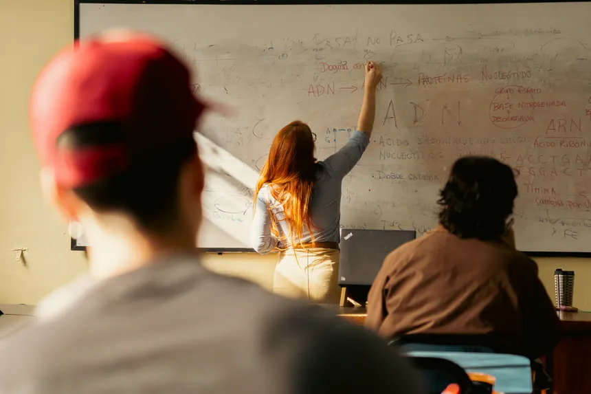 Female teacher writing complex formulas on a whiteboard during a university lecture.
