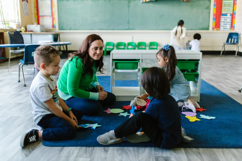 Teacher and children engaged in educational activities on a classroom floor.
