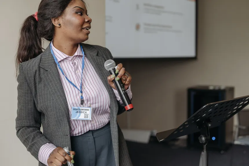 Woman in professional attire presenting at a business seminar with microphone.