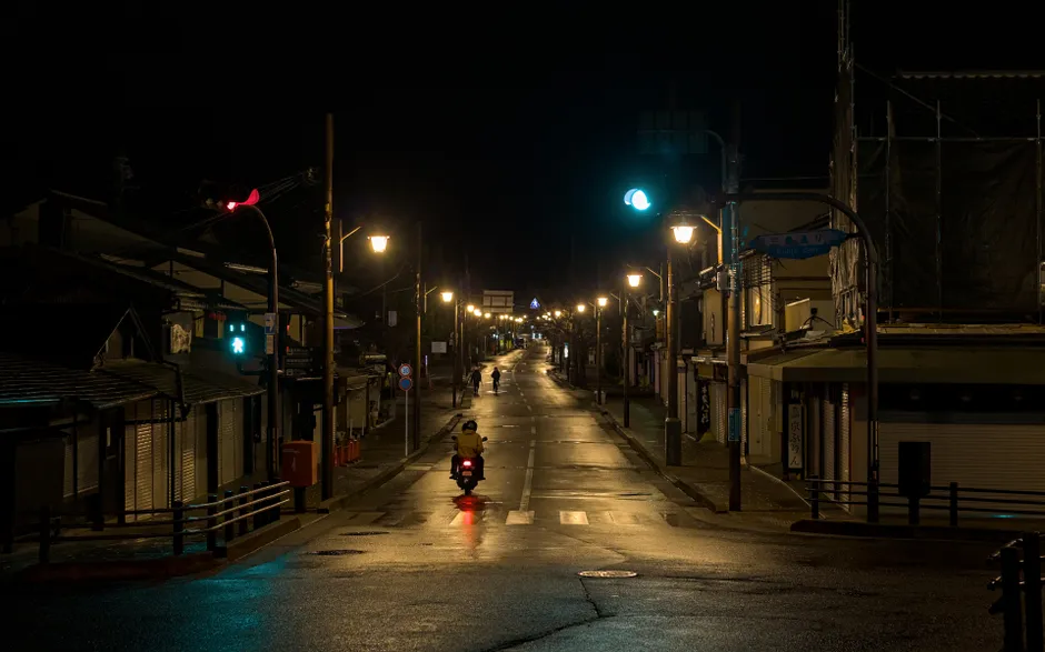 A tranquil night scene in Arashiyama, Kyoto, with streetlights and a lone motorbike.