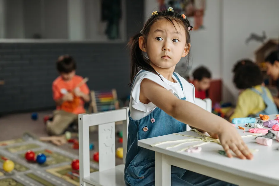 Young girl in classroom exploring creativity with hands-on activities, surrounded by peers.