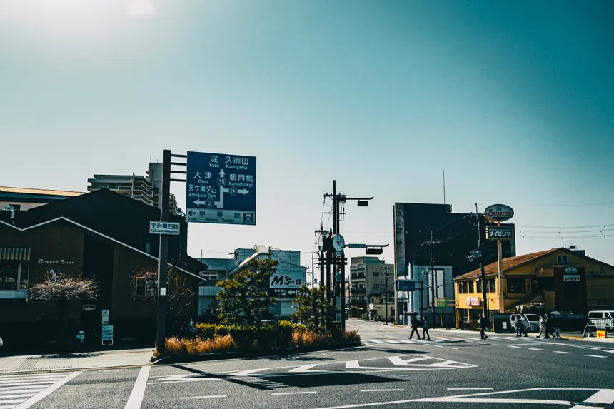 A city street scene featuring buildings, signage, and pedestrians under a bright sky.