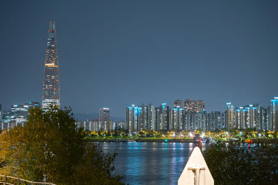 Nighttime view of Seoul city skyline with Lotte World Tower and Han River, featuring vibrant city lights.