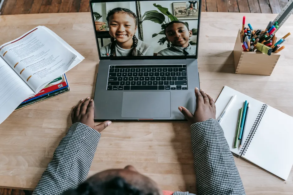 Crop anonymous clever African American female talking with pupils about plan of homework online on laptop