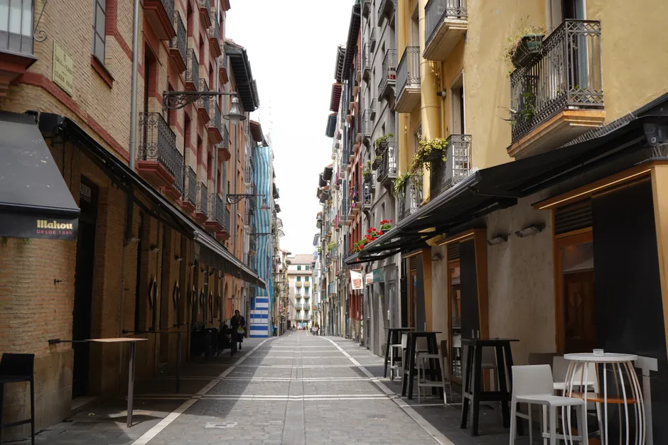 Empty street in Pamplona, Spain, showcasing colorful buildings and outdoor cafes on a bright day.