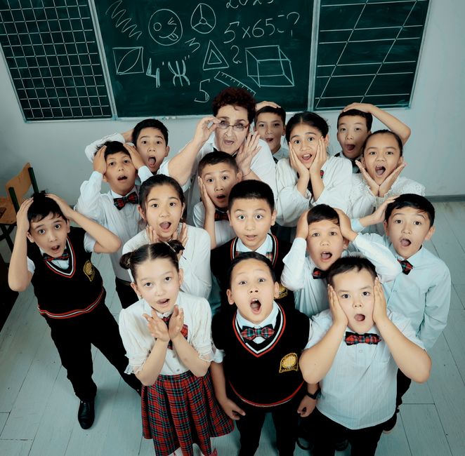 A group of school children in uniforms posing with their teacher inside a classroom.