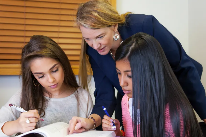 A teacher providing guidance to two students studying in a classroom. Ideal for educational content.