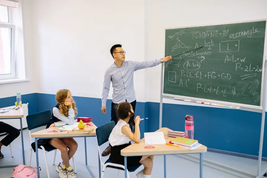 Teacher pointing at chalkboard with students in classroom learning geometry.