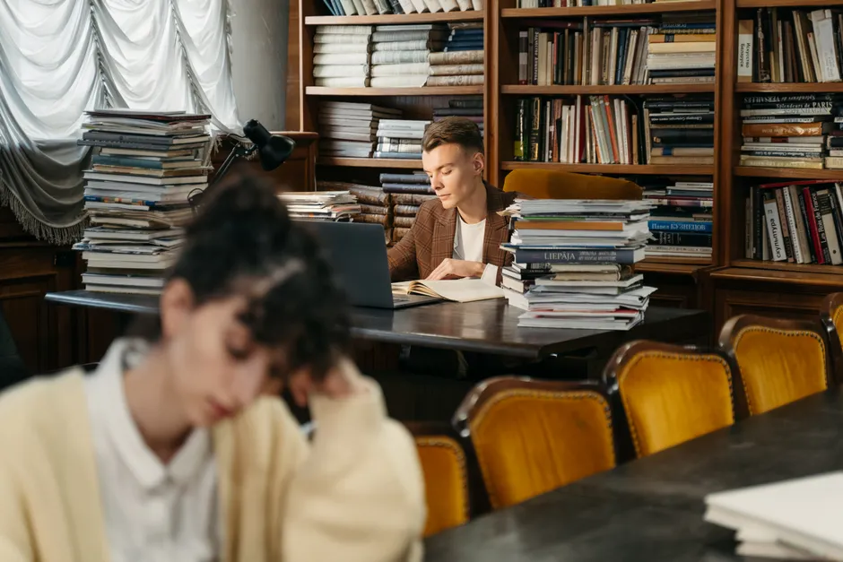 A young man deeply focused while reading in a cozy, well-stocked library.