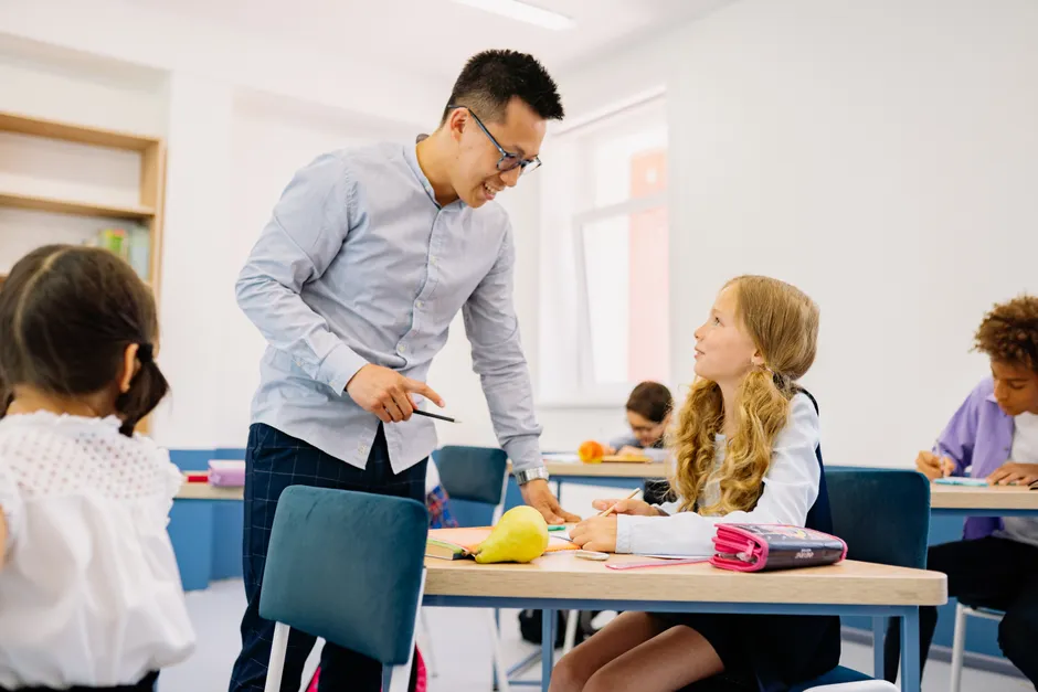 A male teacher interacting with diverse students in a bright classroom setting, promoting active learning.