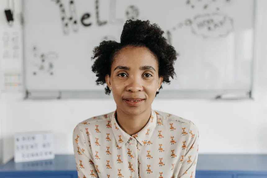 A confident woman with afro hair poses in a classroom, fostering an educational theme.