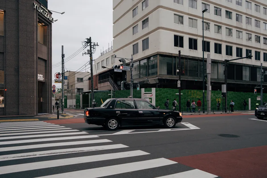 Busy Tokyo intersection with pedestrians and a black taxi on a cloudy day.
