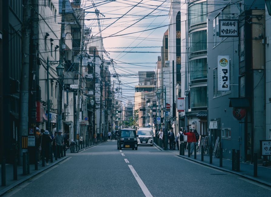 Lively urban street capturing pedestrians, vehicles, and overhead wires in a modern cityscape.