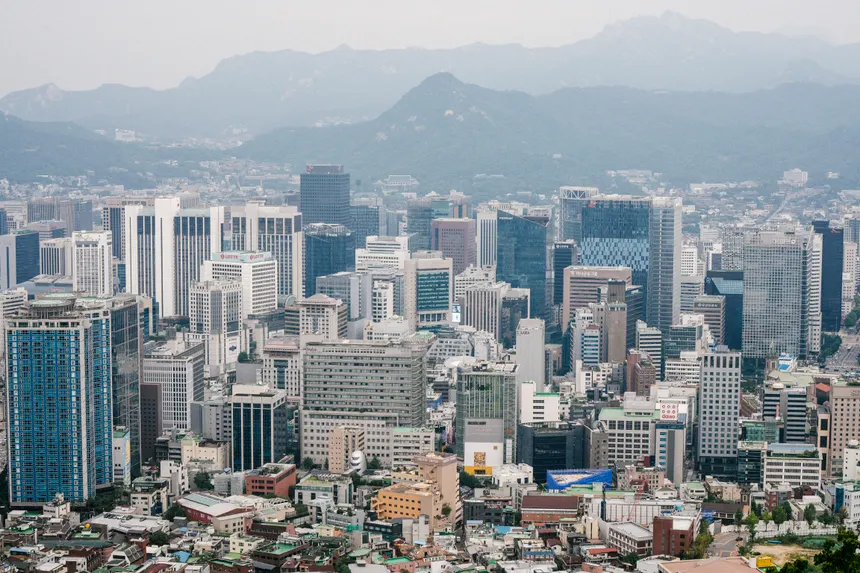 Aerial view of Seoul's skyline featuring modern skyscrapers against mountainous backdrop.